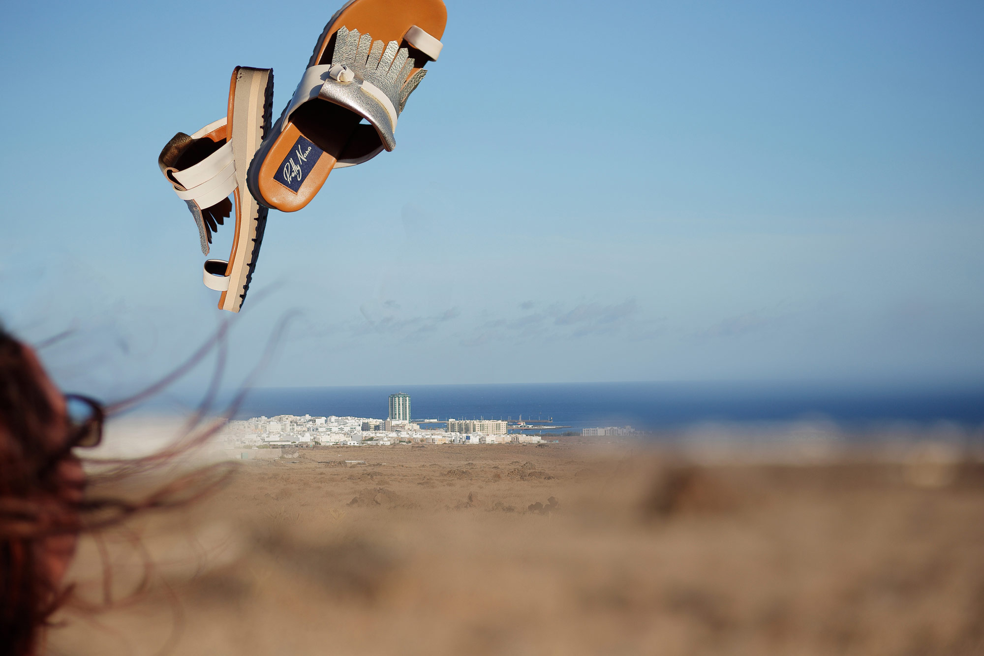 Lanzarote modella lancia in aria sandali argentio sullo sfondo deserto e mare