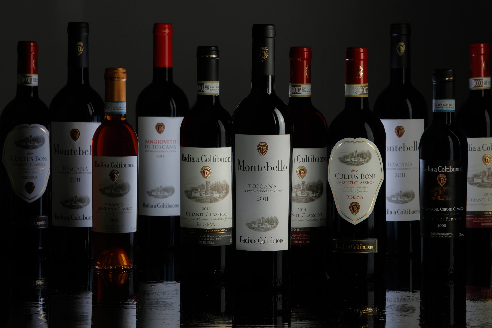 immagine fotografica di una serie di bottiglie di Vino e Vinsanto di Badia a Coltibuono su sfondo scuro